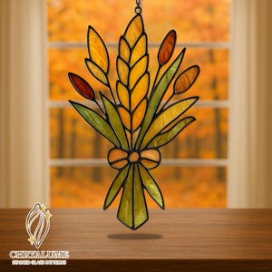 May include: Stained glass bouquet featuring yellow, orange, and green leaves and wheat stalks. The bouquet is tied with an orange bow. The glass is outlined in black and hangs from a chain. The background shows blurred autumn foliage.
