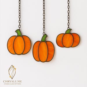 May include: Three orange stained glass pumpkin decorations hanging from dark metal chains. Each pumpkin has a green stem and a dark brown outline. The pumpkins are set against a white background. The logo for Chryalume Stained Glass Patterns is at the bottom.