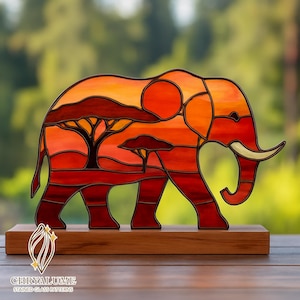 Puede incluir: Escultura de elefante de vidrieras en tonos naranja, rojo y marrón, que representa una escena de la sabana africana. El elefante está montado sobre una base de madera. La escultura presenta un árbol y un sol poniente. El logotipo "CHRYALUME STAINED GLASS PATTERNS" está en la parte inferior.