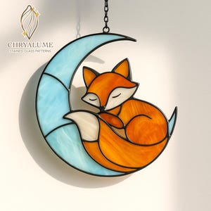 Puede incluir: Un vitral de un zorro naranja y blanco durmiendo sobre una luna creciente azul claro. El zorro y la luna están delineados en negro y suspendidos por una cadena. El texto "CHRYALUME STAINED GLASS PATTERNS" es visible.