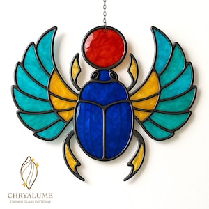 Op de afbeelding: Gebrandschilderde glazen scarabee met blauwe, gele, turquoise en rode panelen, omlijst in zwart. De kever wordt opgehangen door een ketting. De afbeelding bevat de tekst "CHRYALUME STAINED GLASS PATTERNS".