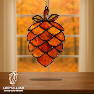 May include: Stained glass pinecone with orange and yellow hues, outlined in black. The decorative piece hangs from a chain. The background shows a window with an autumn scene. The logo "CHRYALUME STAINED GLASS PATTERNS" is visible.