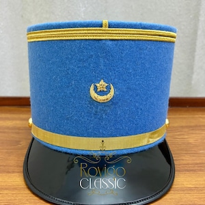 Puede incluir: Un sombrero azul de estilo militar con ribete dorado y ala negra. El sombrero presenta un emblema dorado y el texto "Rovigo CLASSIC". Este sombrero es probablemente una pieza ceremonial o histórica.