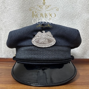 Könnte beinhalten: Marineblaue US Post Official Letter Carrier-Mütze mit glänzendem schwarzem Schirm. Sie hat ein silbernes Abzeichen mit einem Adleremblem und dem Text "US Post Official 1401 Letter Carrier". Das Cap hat ein Mesh-Band und eine schwarze Kordel.