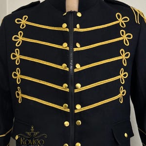 May include: A black military-style jacket with gold trim and buttons. The jacket has decorative gold rope detailing across the chest and shoulders. It features a high collar and a zip closure. The brand name "Rovigo Classic" is visible on the lower left.