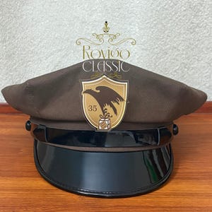 May include: A brown and black cap with a black brim and a brown eagle logo with the text "Rovioo Classic" and "35" on it.