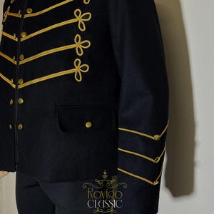 May include: Black military-style jacket with gold trim and buttons. The jacket has gold embroidery on the front and sleeves, and a small pocket. Part of the Rovigo Classic collection. The jacket is a classic design.