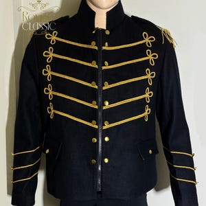 May include: Black military-style jacket with gold trim and accents. The jacket features a high collar, a zip closure, and gold buttons. Gold rope detailing and decorative bows adorn the front and sleeves. The jacket has the text "ROVIGO CLASSIC" on the upper left.