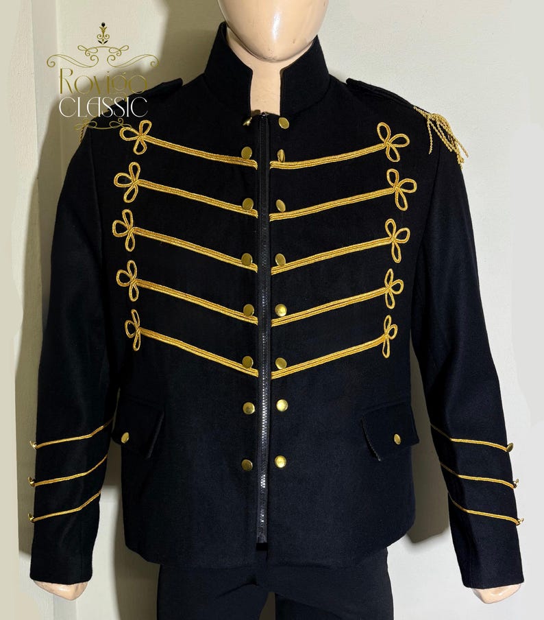 May include: Black military-style jacket with gold trim and accents. The jacket features a high collar, a zip closure, and gold buttons. Gold rope detailing and decorative bows adorn the front and sleeves. The jacket has the text "ROVIGO CLASSIC" on the upper left.