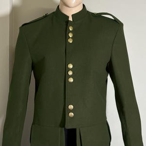 Pode incluir: Uma jaqueta verde escura de estilo militar com botões dourados e gola mandarim. A jaqueta tem uma silhueta longa e ajustada e apresenta um design único com uma bainha curva.