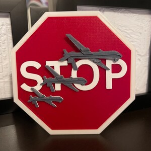 Peut inclure: Un panneau d'arrêt rouge avec l'inscription "STOP" en blanc. Quatre silhouettes de drones grises sont superposées sur le panneau.