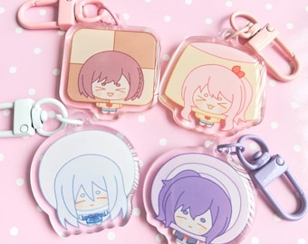 May include: Four colorful anime character keychains with clear acrylic backgrounds and metal clasps. Each keychain features a different character with a unique design and color scheme.