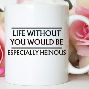 May include: White ceramic mug with the text "LIFE WITHOUT YOU WOULD BE ESPECIALLY HEINOUS" in black and blue lettering. The mug has a curved handle and is set against a background of pink roses.