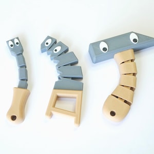 May include: Three toy tools with googly eyes and segmented handles. The tools are a hammer, a saw, and a screwdriver. The tools are made of gray plastic with beige handles.
