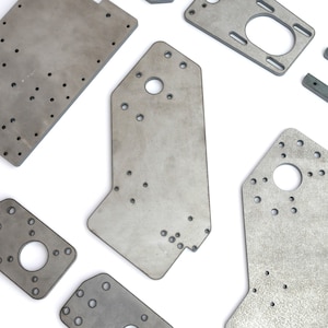 Könnte beinhalten: Ein Satz von fünf Metallplatten in verschiedenen Formen und Größen. Jede Platte hat mehrere Löcher, die hineingebohrt wurden. Die Platten sind alle silberfarben und haben eine raue, unfertige Textur.