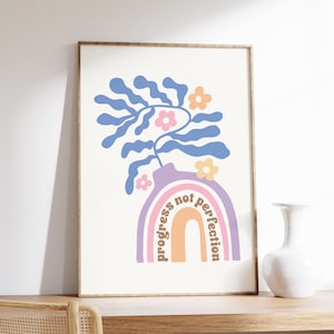 Puede incluir: Una impresión enmarcada con un diseño de arcoíris y el texto "progress not perfection" en letras marrones. El arcoíris está en tonos de rosa, morado y naranja. Una planta estilizada azul con flores rosas y amarillas está en un jarrón morado encima del arcoíris.