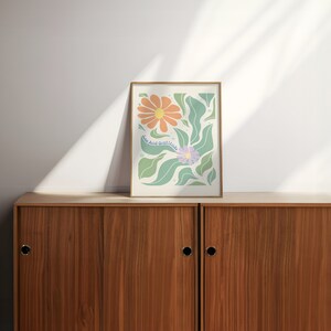 May include: A framed print with a floral design featuring orange and purple flowers with green leaves. The print has the text "Love And Gratitude" in a light blue font.