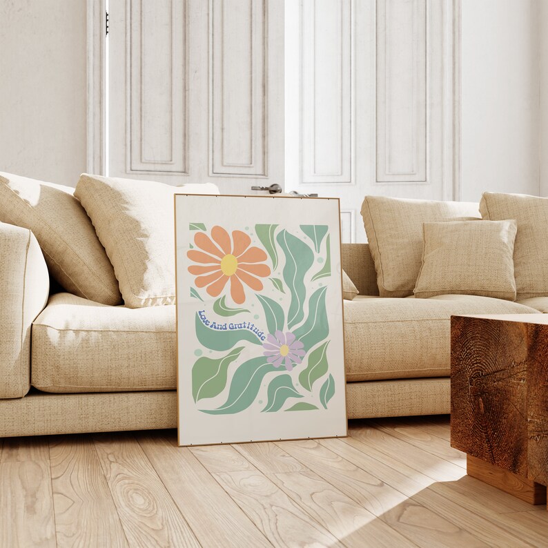 May include: A framed print with a white background featuring two stylized flowers in shades of orange, pink, and purple. The flowers are surrounded by green leaves and the text "Love And Gratitude" is written in blue.