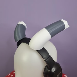 Peut inclure: Une paire de coussinets d'oreille imprimés en 3D, blancs et gris, pour casque audio. Les coussinets d'oreille sont fixés à un casque audio noir.