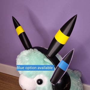 May include: A plush toy with black and yellow ears and a black headband with a blue and black ear on the right side. The toy is wearing a black headset with the text "Creative Sound" on the side.  Blue option available.
