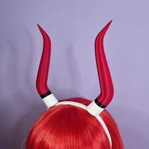 Op de afbeelding: Rood duivelshoorn haarband met een witte band. Het haarband zit op een rood pruik.