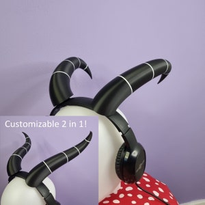 Puede incluir: Auriculares negros con rayas blancas en la diadema, que se asemejan a cuernos. Los auriculares son personalizables y se pueden usar como diadema o como auriculares. El texto "Customizable 2 in 1!" es visible en la imagen.