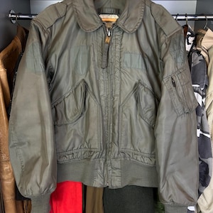 May include: A green bomber jacket with a zip fastening and two pockets. The jacket has a ribbed collar, cuffs, and waistband.