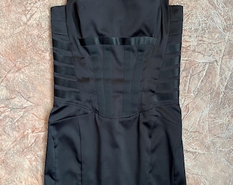 May include: A black satin dress with a square neckline and wide shoulder straps. The bodice features vertical and horizontal pleating details, creating a structured silhouette. The dress has a fitted waist and a straight skirt.