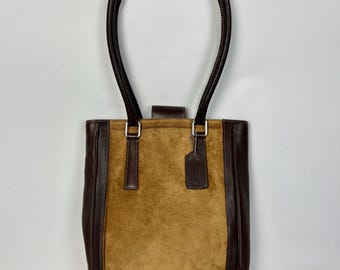 May include: A brown leather tote bag with a suede front panel and a Coach brand tag. The bag has two top handles and a rectangular shape.
