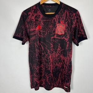 May include: A red and black soccer jersey with a red and gold crest featuring a coat of arms and the text "FÚTBOL" on the front. The jersey has a black and red marbled pattern and the Adidas logo on the left chest.