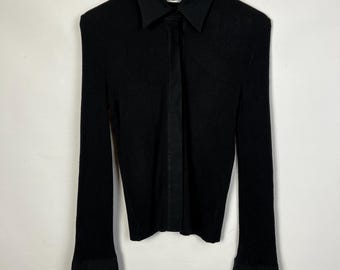 May include: Black long-sleeve shirt with a collared neckline and flared cuffs. The shirt is made of a ribbed knit fabric with a contrasting smooth panel down the front. The cuffs and collar are a smooth, solid black material.
