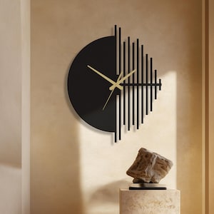 May include: A contemporary black wall clock with gold hands and a distinctive geometric pattern. The clock is mounted on a beige wall. Beneath the clock is a stone sculpture on a square, textured pedestal. The room has a warm, neutral colour palette.