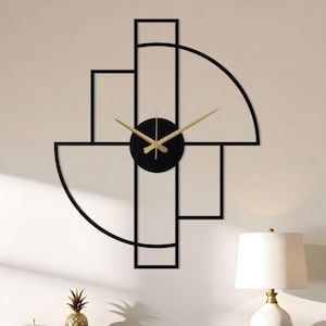 May include: A contemporary wall clock with a black geometric frame and a circular clock face. The clock has gold-coloured hands and is mounted on a white wall. The design incorporates rectangular and semi-circular shapes. A black dresser and lamp are in the foreground.