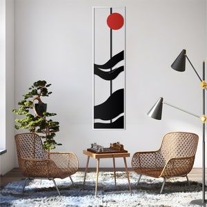 May include: A black and white abstract wall art piece with a red circle in the center. The art is framed and hanging on a white wall. Two wicker chairs and a small table with a chessboard are in the foreground.