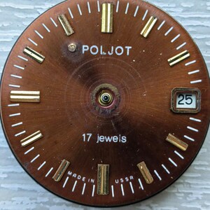 May include: A vintage watch face with a copper-colored dial. The face features gold-colored hour markers and hands, with the brand name "POLJOT" in white. The text "17 jewels" and "MADE IN USSR" are also visible. The date is displayed as "25".