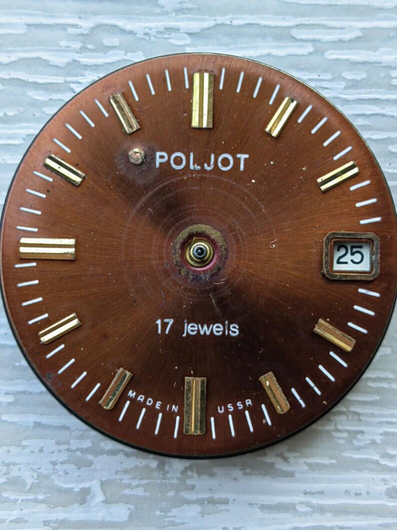 May include: A vintage watch face with a copper-colored dial. The face features gold-colored hour markers and hands, with the brand name "POLJOT" in white. The text "17 jewels" and "MADE IN USSR" are also visible. The date is displayed as "25".