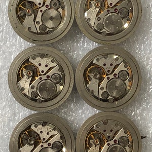 May include: Six silver-coloured watch movements with intricate gears and a gold-coloured winding stem. The movements are labelled with the number "2214".