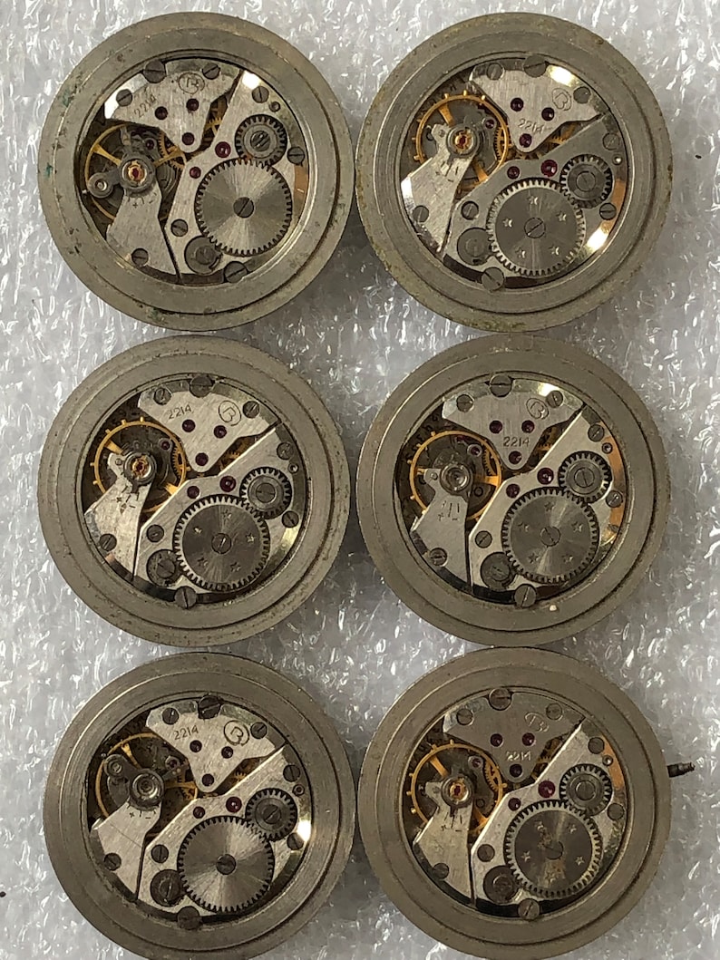 May include: Six silver-coloured watch movements with intricate gears and a gold-coloured winding stem. The movements are labelled with the number "2214".