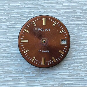 May include: A vintage watch face with a brown dial and gold-colored hour markers and hands. The watch face has the brand name "POLJOT" and the text "17 jewels". The date is displayed as "25".