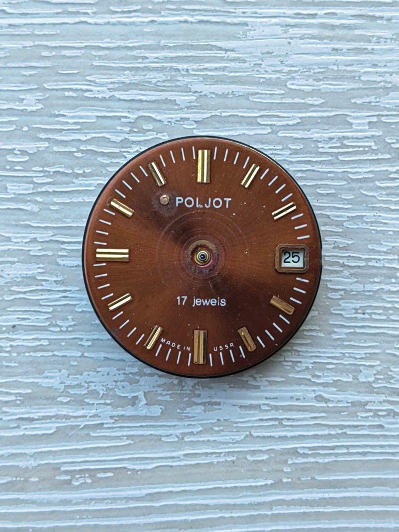 May include: A vintage watch face with a brown dial and gold-colored hour markers and hands. The watch face has the brand name "POLJOT" and the text "17 jewels". The date is displayed as "25".