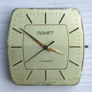 May include: A vintage square clock face with a gold-colored finish. The clock face features the word "ПОЛЕТ" in Cyrillic script, along with the text "17 KAMHEЙ" and "СДЕЛАНО В СССР". The clock hands are gold and black.