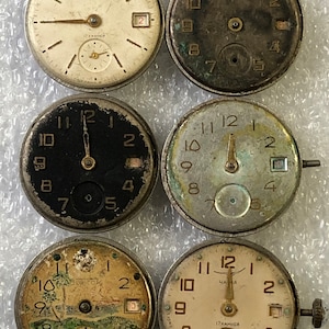 Peut inclure: Six cadrans de montres vintage avec des designs différents. Les cadrans sont tous ronds et ont des chiffres et des aiguilles noirs. Certains cadrans ont un guichet de date. Les cadrans sont tous dans différents états d'usure.