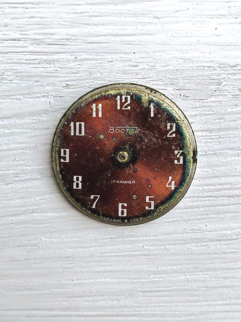 May include: A vintage watch face with a rusty brown dial and white numerals. The face has the text "Восток" and "17 KAMHEЙ". The watch face is round with a gold-colored metal rim.