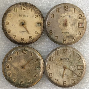 Könnte beinhalten: Vier Vintage-Zifferblätter mit römischen Ziffern. Die Zifferblätter sind alle silberfarben mit schwarzen Markierungen und tragen den Schriftzug "Vostok". Die Zifferblätter sind alle leicht abgenutzt und haben eine Patina.