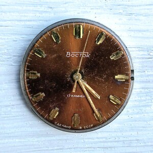 May include: A vintage watch face with a copper-colored dial and gold-toned hour markers. The watch face has the word "Восток" in white lettering and the text "17 камней" and "Сделано в СССР".
