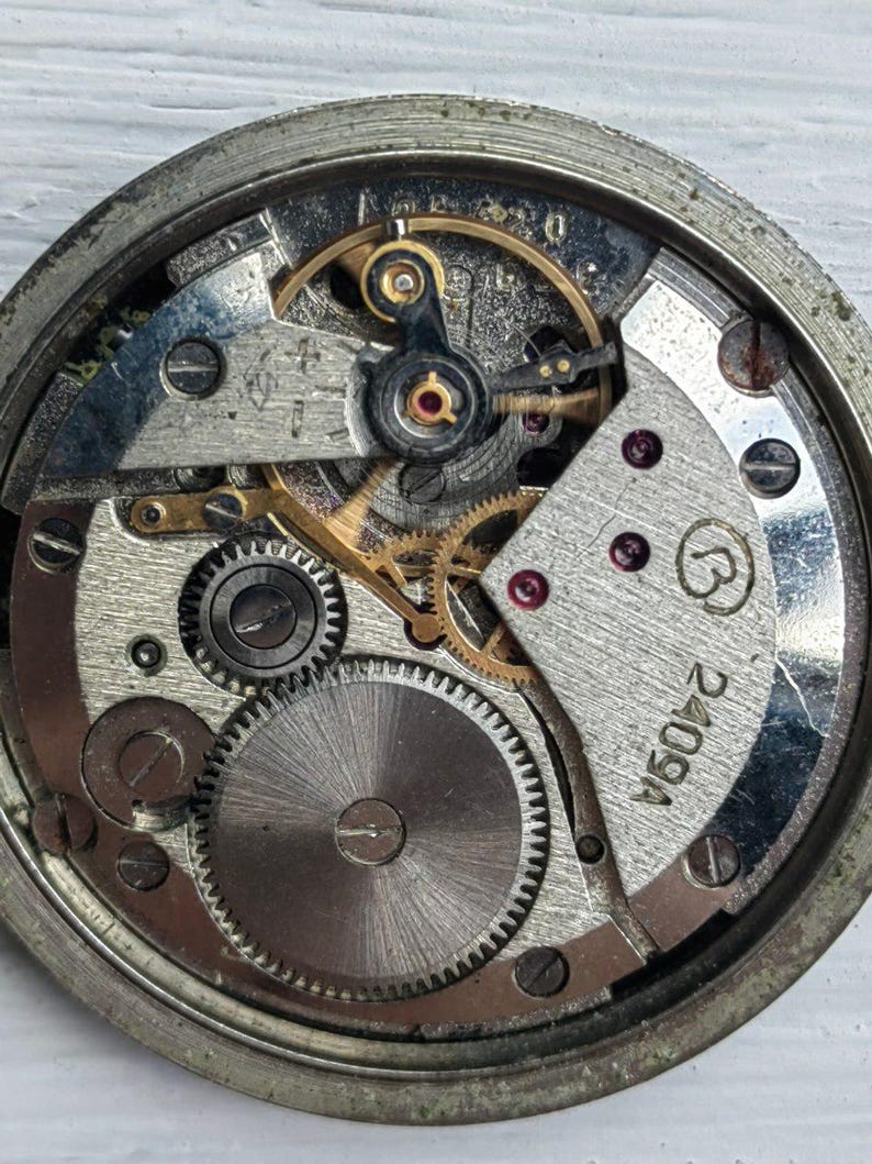 May include: Close-up of a vintage watch movement, showcasing intricate gears, springs, and other mechanical components. The watch's internal mechanism is visible, with a silver and gold color scheme. The watch face is not present, revealing the inner workings.