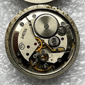 May include: Close-up of two watch movements, showcasing intricate gears and mechanisms. The lower movement features the number "2409A" and a circular symbol. The gears are silver and gold, set within a circular metal frame.