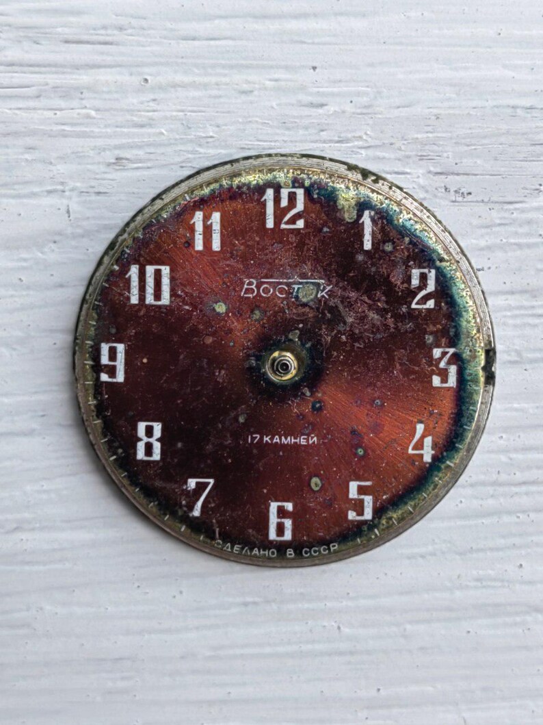 May include: Vintage watch face with a dark red and bronze color scheme. White numerals mark the hours, with the brand name "Восток" and text "17 камней" and "СДЕЛАНО В СССР" visible. The face has a circular shape with a metallic rim.