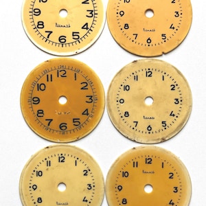 May include: Six vintage clock faces with a cream and yellow color scheme. Each face has black numerals, minute markers, and a central hole. The word "Rumash" is printed on each face. These clock faces are ideal for craft projects.