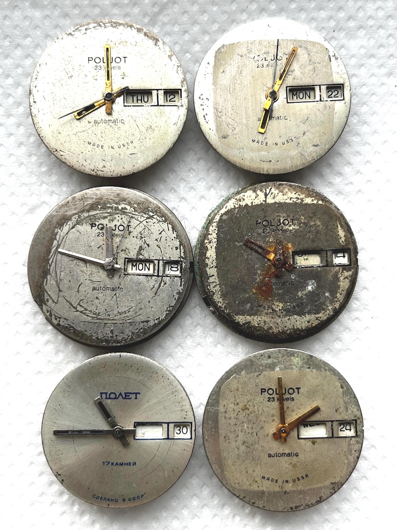 May include: Six vintage watch faces with visible wear and tear. The faces are round, with gold-toned hands and markers. Some display the day and date. The text "POLJOT" and "automatic" are visible on some faces. The text "MADE IN USSR" is also visible.